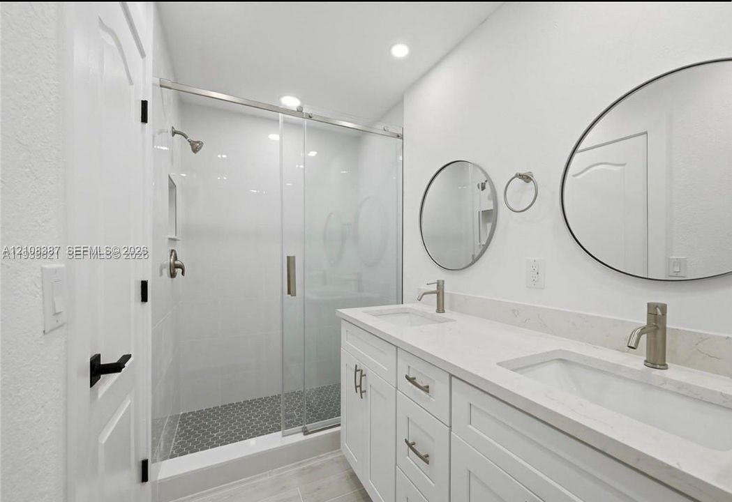 Dual vanity with white cabinetry, stone-surface countertop, and dual round mirrors