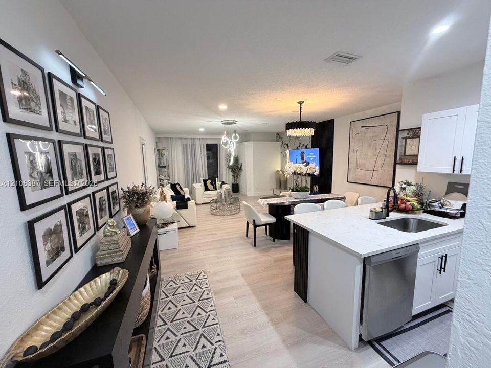 Open-concept kitchen featuring an island with quartz countertop, white shaker-style cabinetry, matte black hardware, and wood-finish flooring