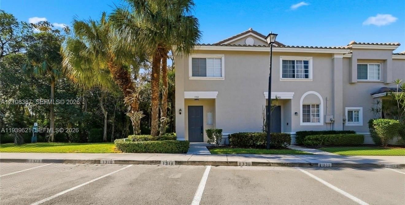 Two-story exterior featuring a neutral stucco facade, tile roofing, decorative arched window detailing, and integrated landscape hedging