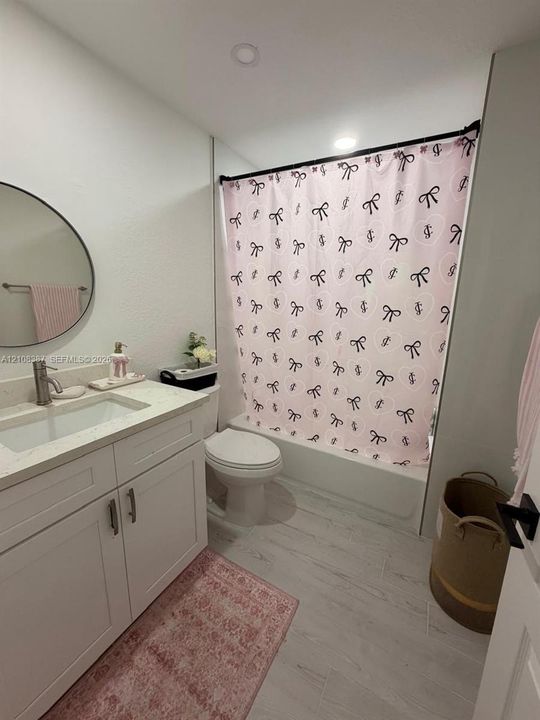 White shaker-style vanity with a solid surface countertop, integrated sink, circular wall-mounted mirror, and tile flooring