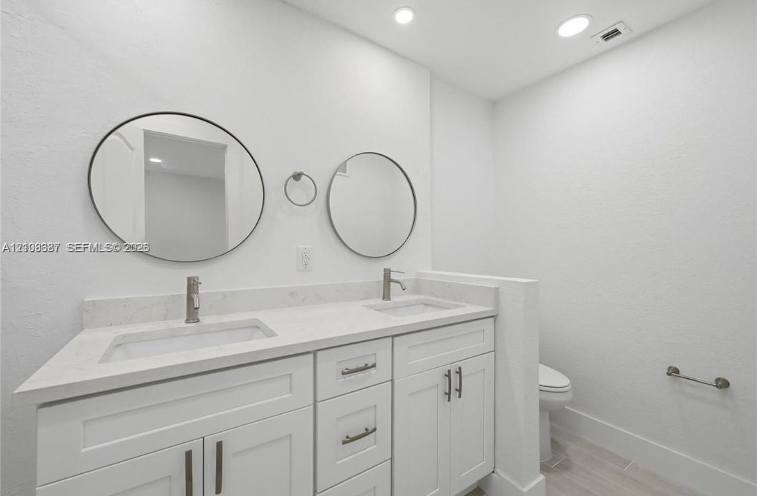 Dual-sink vanity featuring white cabinetry, stone-finish countertops, circular wall-mounted mirrors, and chrome-finish faucets