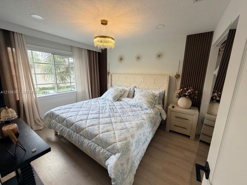 Bedroom featuring recessed ceiling lighting, a circular tiered crystal chandelier, wood-finish flooring, and vertical wood-slat accent wall detailing