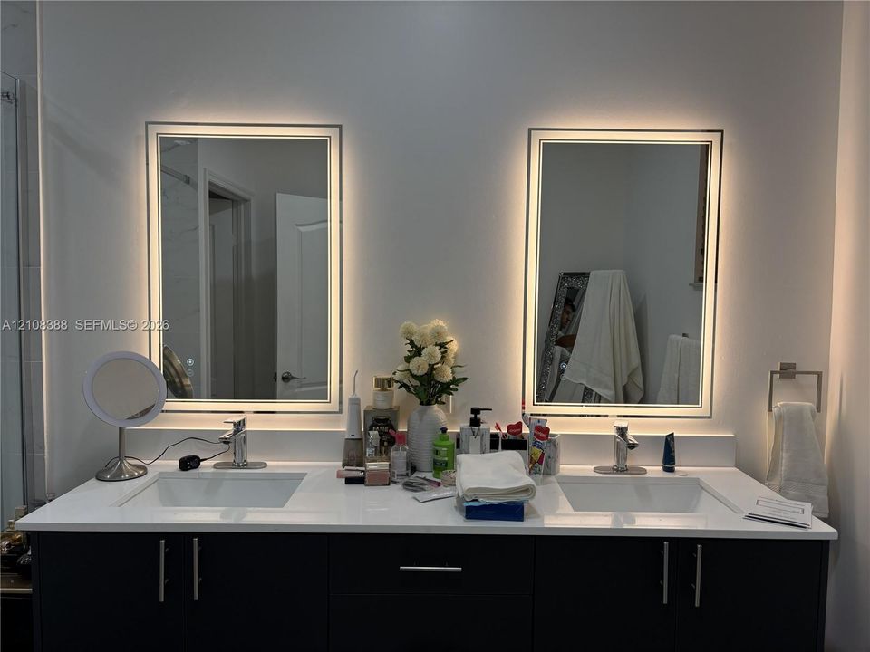 Dual-sink vanity featuring a white solid-surface countertop, dark cabinetry, and two integrated LED-backlit rectangular mirrors