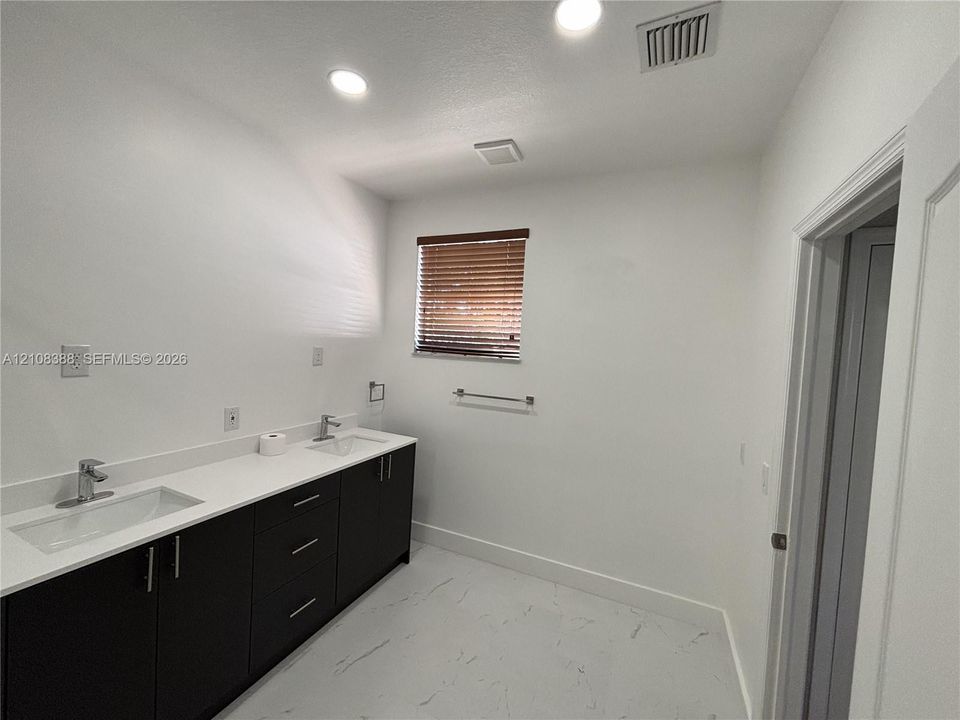 Double vanity featuring dark cabinetry, solid surface countertops, dual undermount sinks with chrome fixtures, and stone-finish flooring