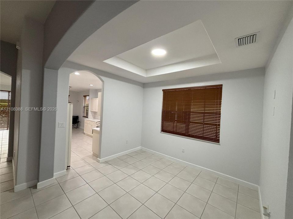 Open-concept interior featuring large-format ceramic tile flooring, arched wall cutouts, white cabinetry, a breakfast bar, and recessed lighting