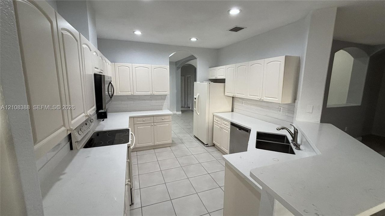 Open floor plan featuring arched architectural cutouts, neutral ceramic tile flooring, and tray ceiling detail