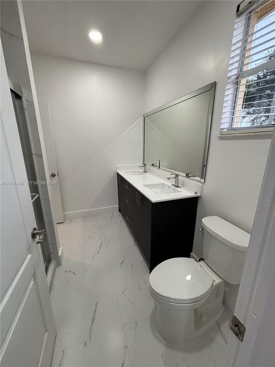 Dual-sink vanity with white stone-finish countertop, full-width mirror, and large-format tile flooring with veining detail