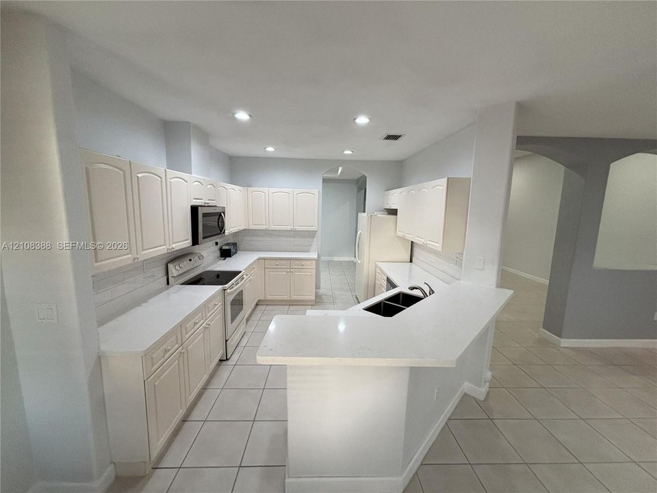 Kitchen featuring white cabinetry, solid surface countertops, a dual-basin sink with a chrome faucet, recessed lighting, and tile flooring