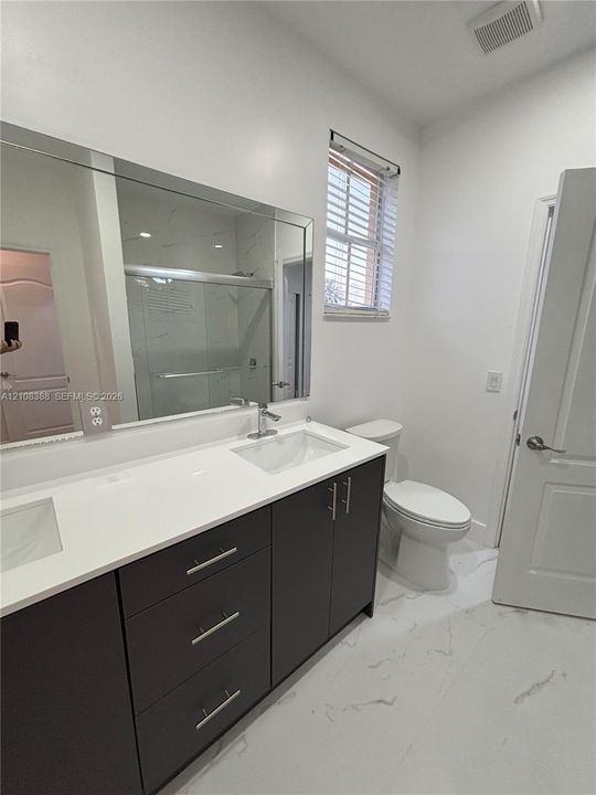 Dual-sink vanity with dark cabinetry, white countertop, large wall-mounted mirror, and tile flooring