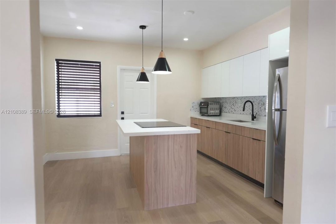Kitchen featuring two-tone cabinetry, wood-finish island with integrated cooktop, quartz countertops, patterned tile backsplash, and matte black plumbing fixtures