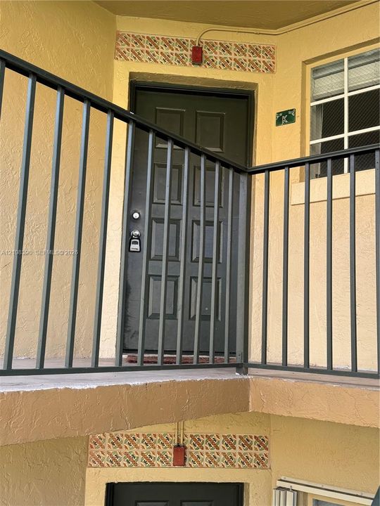 Exterior entry featuring a multi-panel door, metal balcony railing, and decorative tile accents