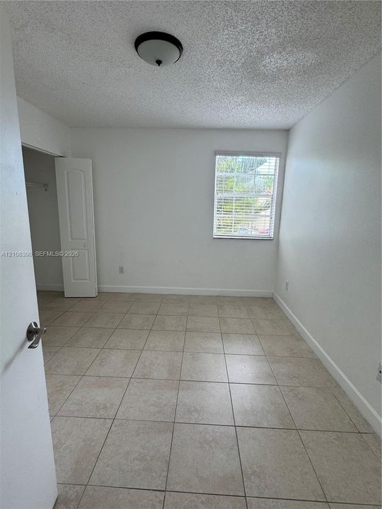 Room featuring neutral-tone tile flooring, a single-panel interior door, a built-in closet, and a window with horizontal blinds