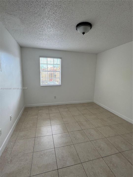 Interior space featuring large-format ceramic tile flooring, neutral wall tones, a single-pane window with internal grids, and a central dome-style ceiling light fixture
