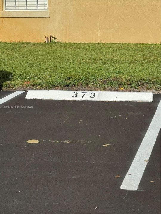 Assigned parking space featuring painted concrete wheel stop, asphalt surface, and painted stall demarcations