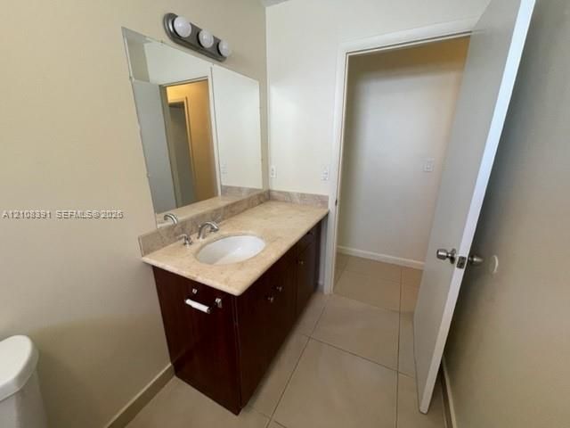 Vanity featuring a stone countertop with an integrated basin, wood-finish cabinetry, a large wall-mounted mirror, three-light fixture, and neutral tile flooring