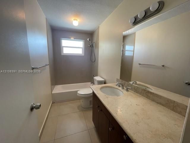 Bathroom featuring a stone-topped vanity with an integrated basin, large wall-mounted mirror, light-colored tile flooring, and a combined tub and shower unit