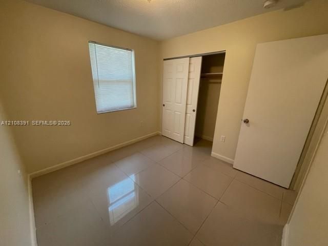 Neutral-toned ceramic tile flooring, sliding bifold closet doors, and a window with integrated blinds