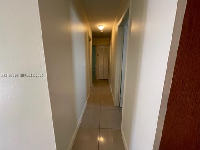 Interior hallway featuring neutral-toned tile flooring, smooth wall finishes, and bifold closet doors