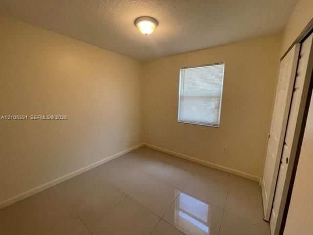 Room featuring neutral wall paint, tile flooring, a window with horizontal blinds, a ceiling-mounted light fixture, and a built-in closet with sliding doors
