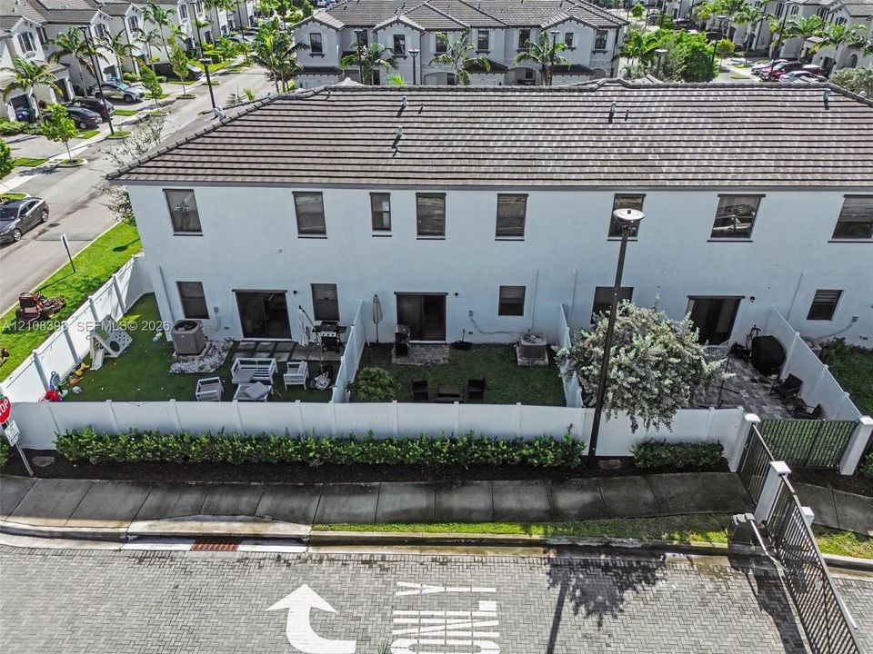 Two-story townhouse exterior featuring white stucco siding, a tiled roof, private fenced rear yards with patio pavers, and manicured landscaping