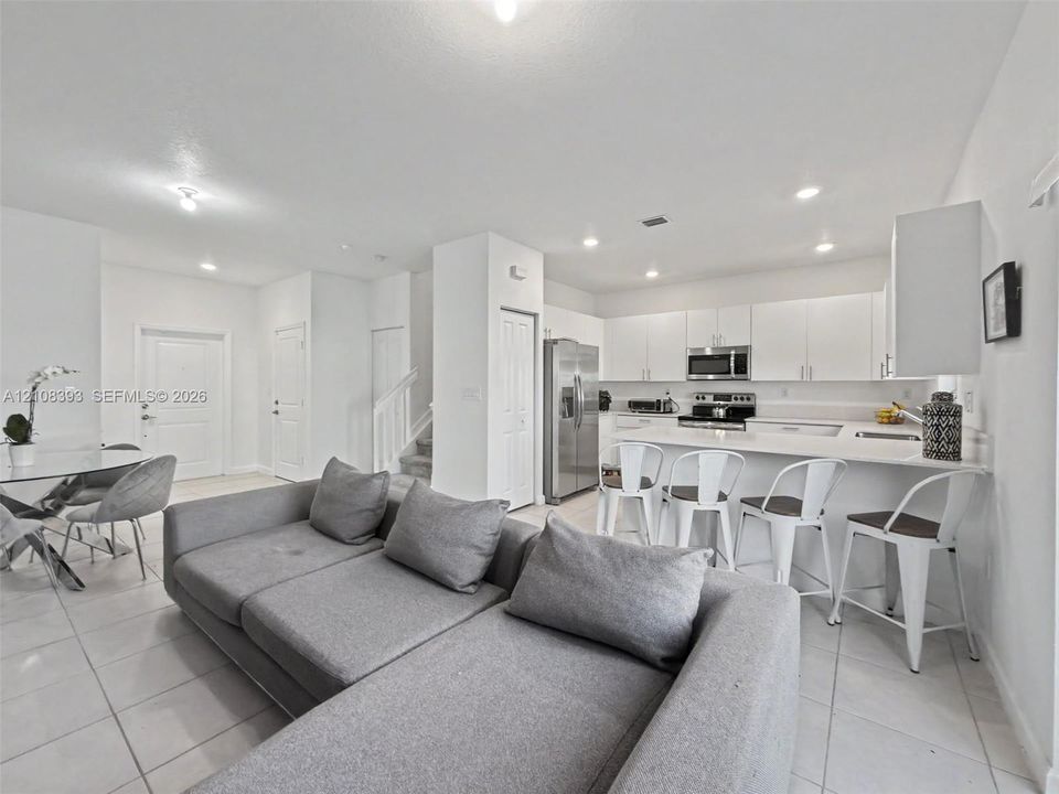 Open-concept kitchen featuring white cabinetry, a spacious central island with bar seating, stainless steel appliances, and neutral tile flooring throughout