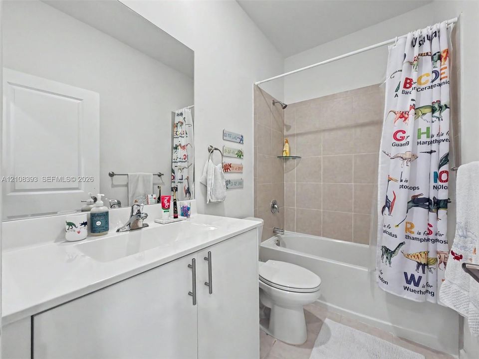 Full-width vanity with integrated sink and chrome faucet, large vanity mirror, and bathtub featuring neutral-toned tile surround