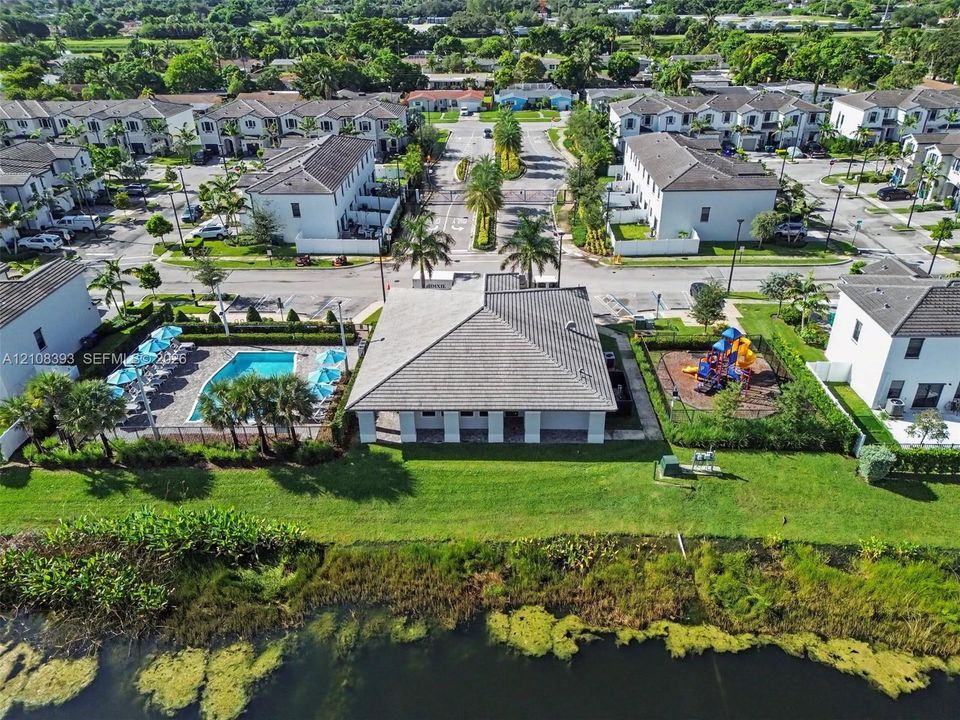 Community facility featuring a tile roof, an outdoor swimming pool, a fenced play structure, and expansive green space positioned along a waterfront