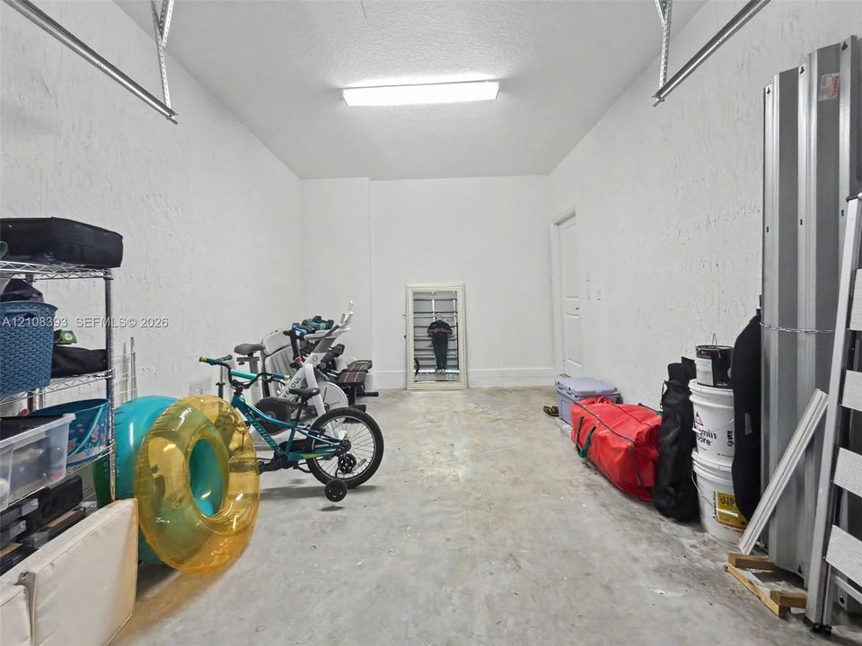 Enclosed garage featuring concrete flooring, textured walls, and overhead LED lighting