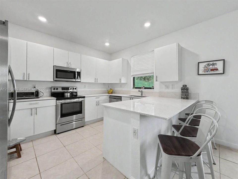 Kitchen featuring white flat-panel cabinetry, a peninsula with stone-finish countertops, stainless steel appliances, and large-format tile flooring
