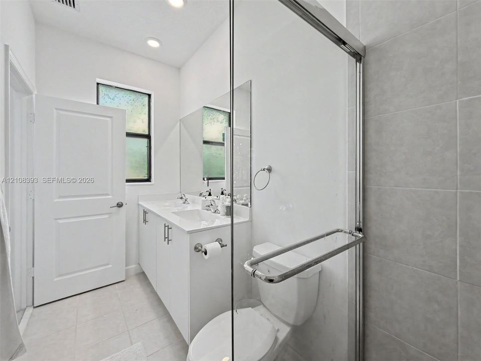Double vanity with integrated sinks, white cabinetry, polished chrome hardware, and glass-enclosed shower with large-format tile surround