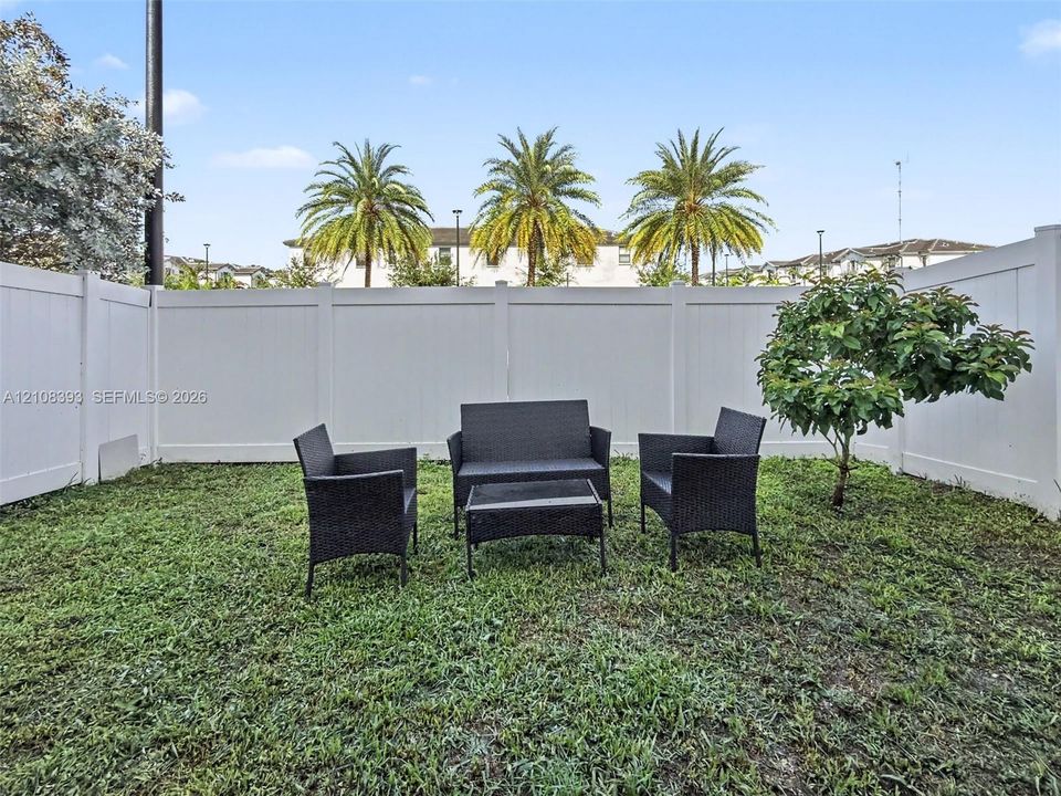 Enclosed backyard featuring white vinyl privacy fencing and a mature tree