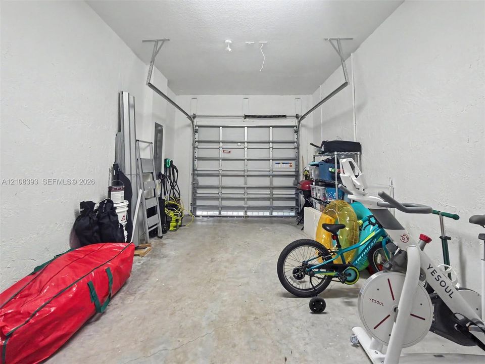 Single-car garage featuring a metal roll-up door, exposed ceiling rafters, and concrete flooring