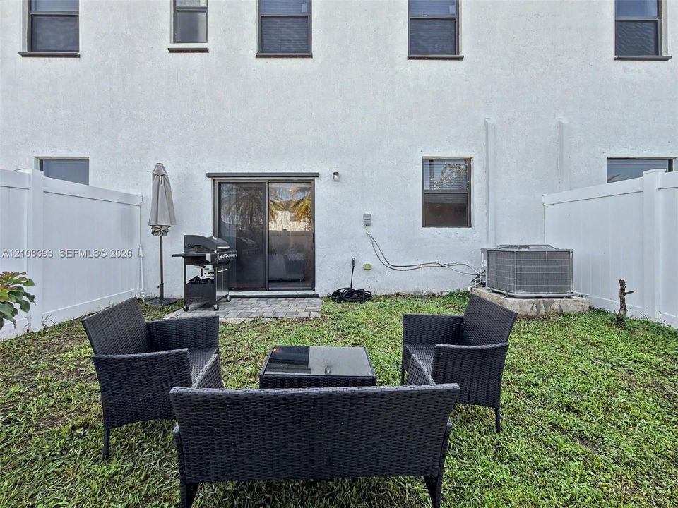 Fenced backyard featuring a paved patio, exterior sliding glass door, and green space