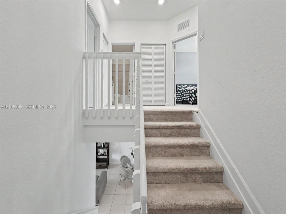 Staircase featuring neutral carpeting, white wooden balustrades, recessed ceiling lighting, and louvered closet doors