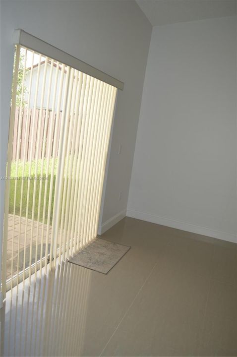Sliding glass door with vertical blinds, neutral tile flooring, and exterior paver patio