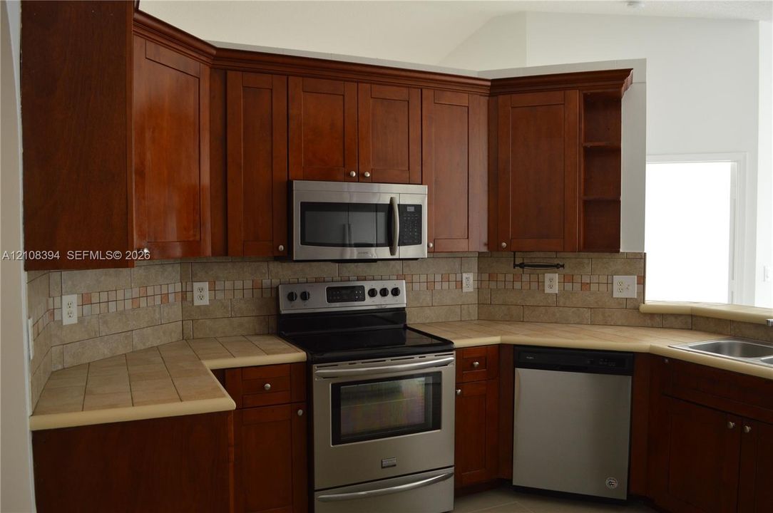 Kitchen featuring wood cabinetry, tiled countertops, stainless steel appliances, and a decorative tile backsplash