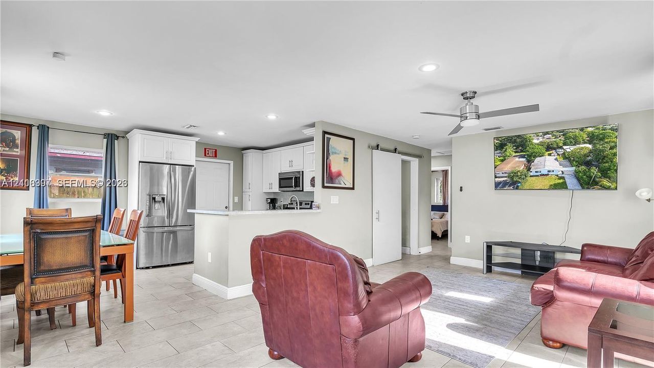 Open-concept floor plan featuring light-toned tile flooring, recessed lighting, white cabinetry, stainless steel refrigerator, and a sliding barn door