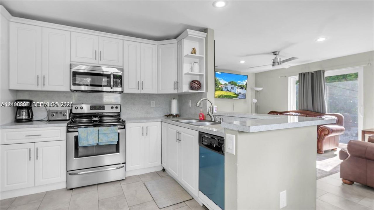 Kitchen featuring white cabinetry, stone-finish countertops, stainless steel appliances, a peninsula with a double-basin sink, and tile flooring