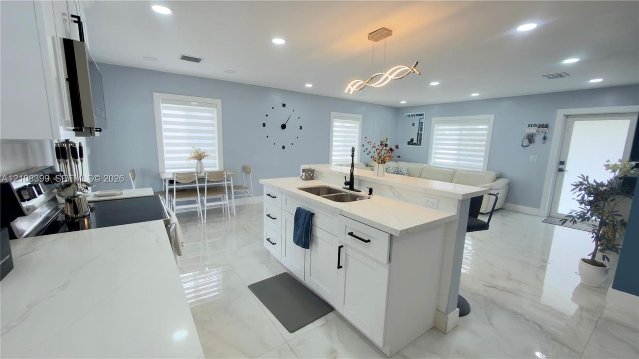 Kitchen featuring white shaker-style cabinetry, quartz countertops, a central island with a double-basin undermount sink, recessed lighting, and tile flooring