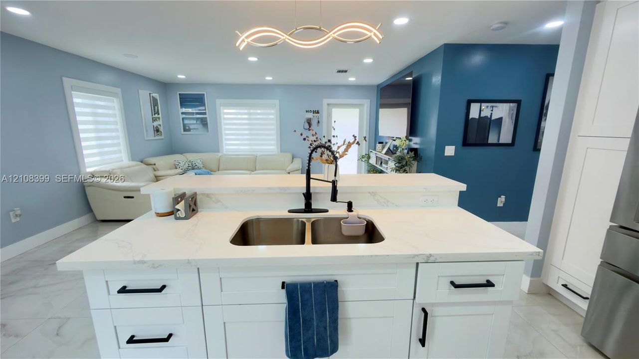 Kitchen island featuring white cabinetry, quartz-style countertops, an undermount double-basin stainless steel sink, and a matte black gooseneck faucet