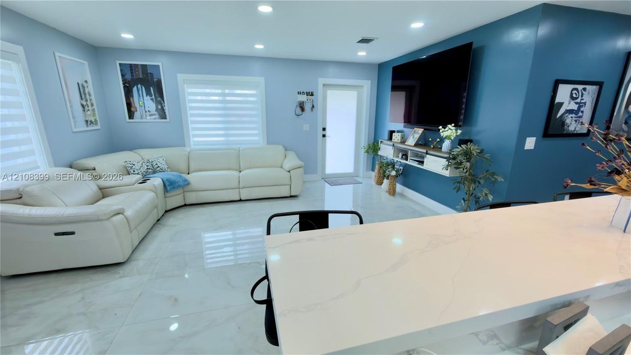 Open-concept living space featuring light-toned large-format tile flooring, recessed lighting, and a built-in floating media console