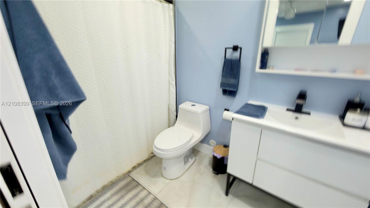 Modern vanity with integrated basin, matte black faucet, and sleek white cabinetry, paired with a contemporary one-piece toilet and light-toned tile flooring