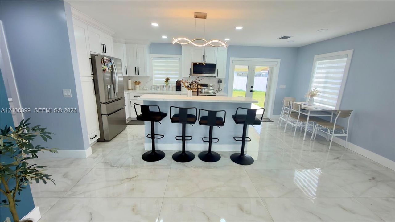 Kitchen featuring white cabinetry, a center island with a stone-surface countertop, stainless steel appliances, large-format tile flooring, and a modern sculptural light fixture
