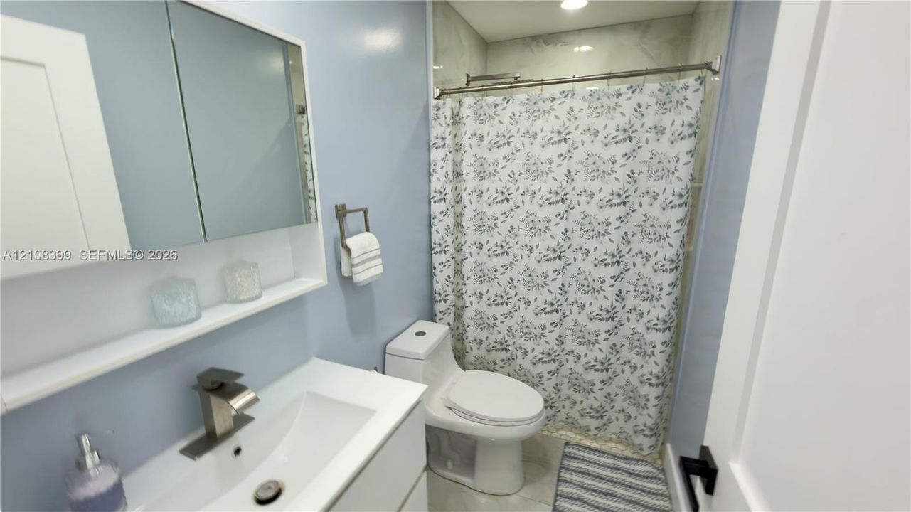 Bathroom featuring a floating vanity with a white countertop and rectangular basin, brushed-nickel faucet, built-in medicine cabinet, and a tiled shower surround