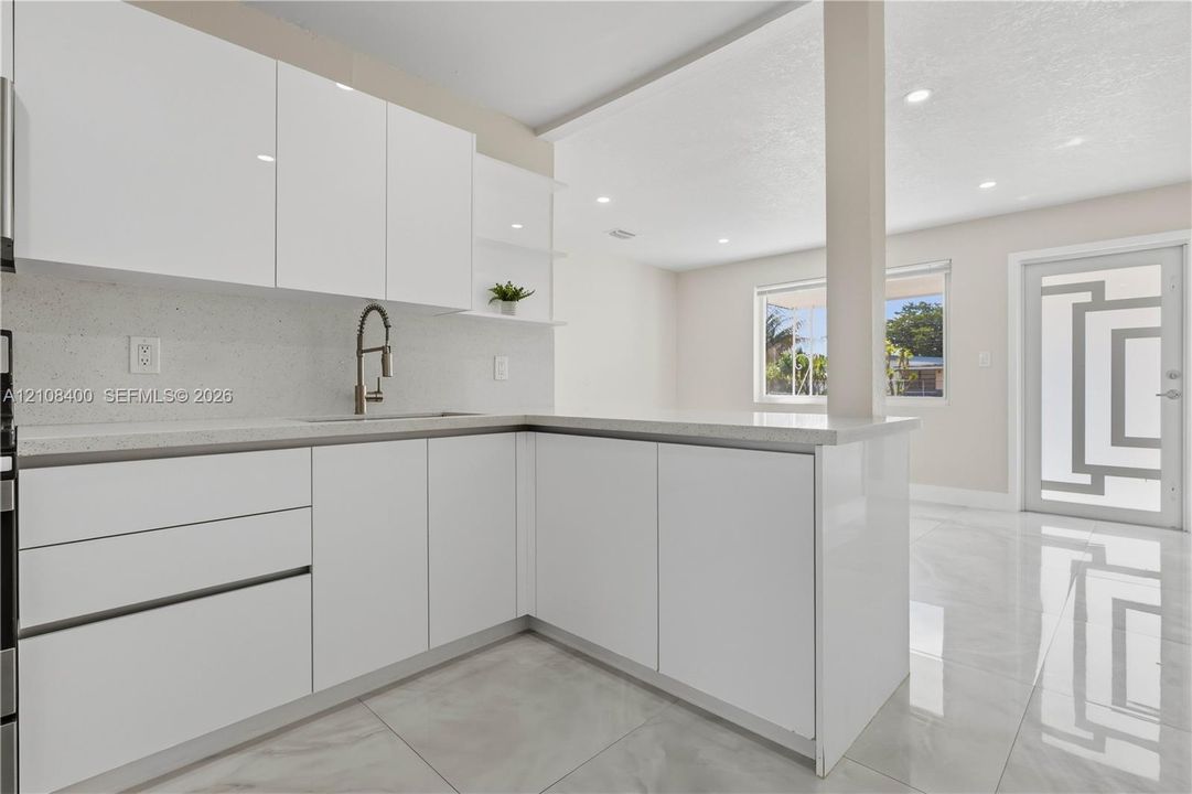 Kitchen featuring high-gloss white cabinetry, quartz countertops, a gooseneck faucet, large-format tile flooring, and a glass-paneled exterior door