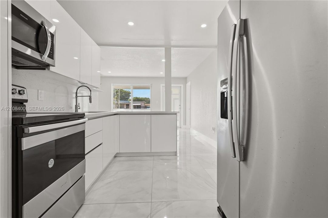 Kitchen featuring high-gloss white cabinetry, stainless steel appliances, recessed lighting, and large-format tile flooring