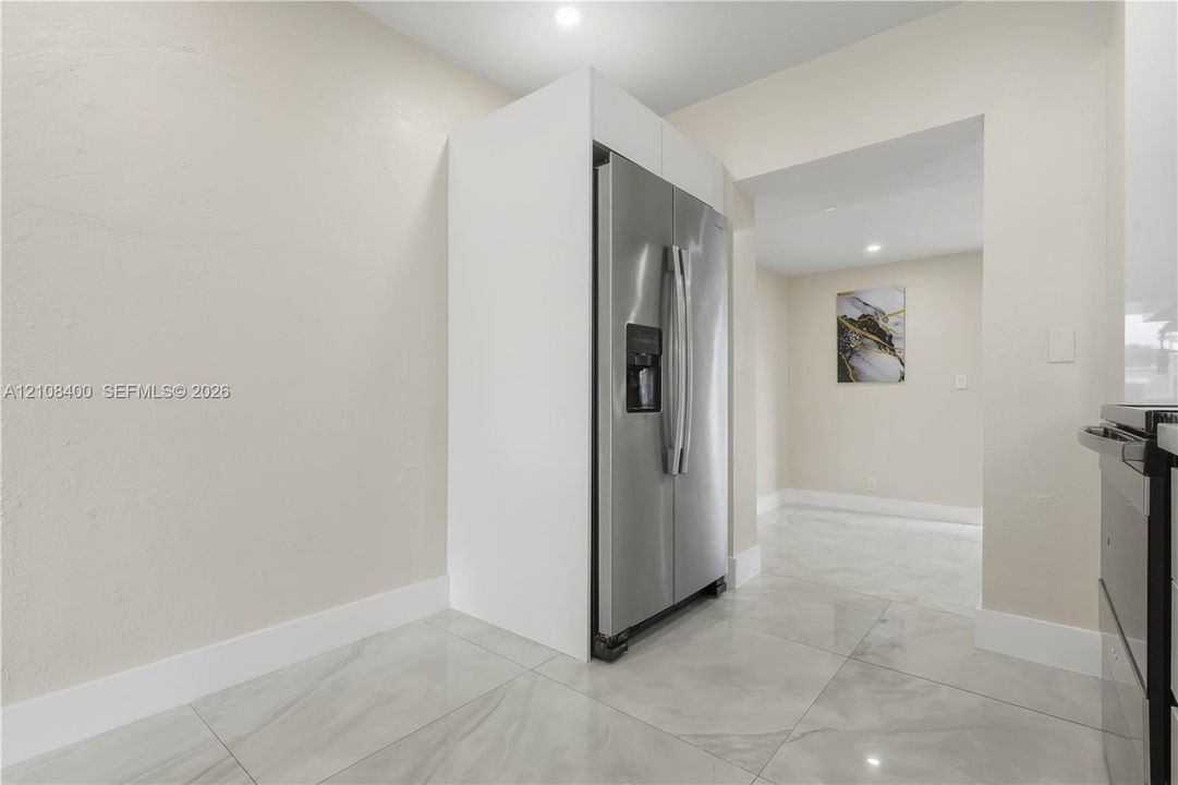 Stainless steel side-by-side refrigerator, white built-in cabinetry surround, and large-format tile flooring