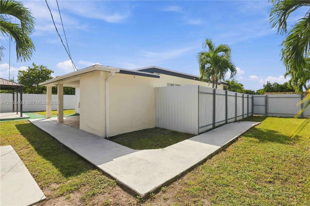 Backyard featuring a covered concrete patio, perimeter vinyl fencing, and a concrete pathway