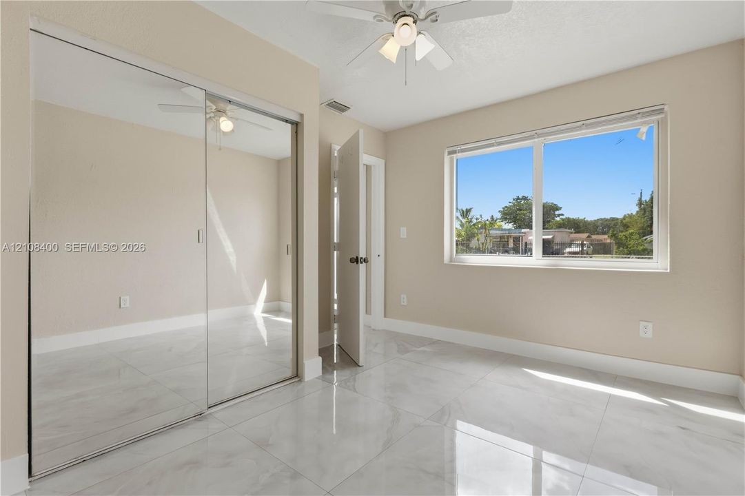 Room with high-gloss polished tile flooring, mirrored sliding closet doors, a neutral color palette, a multi-light ceiling fan, and a large horizontal window