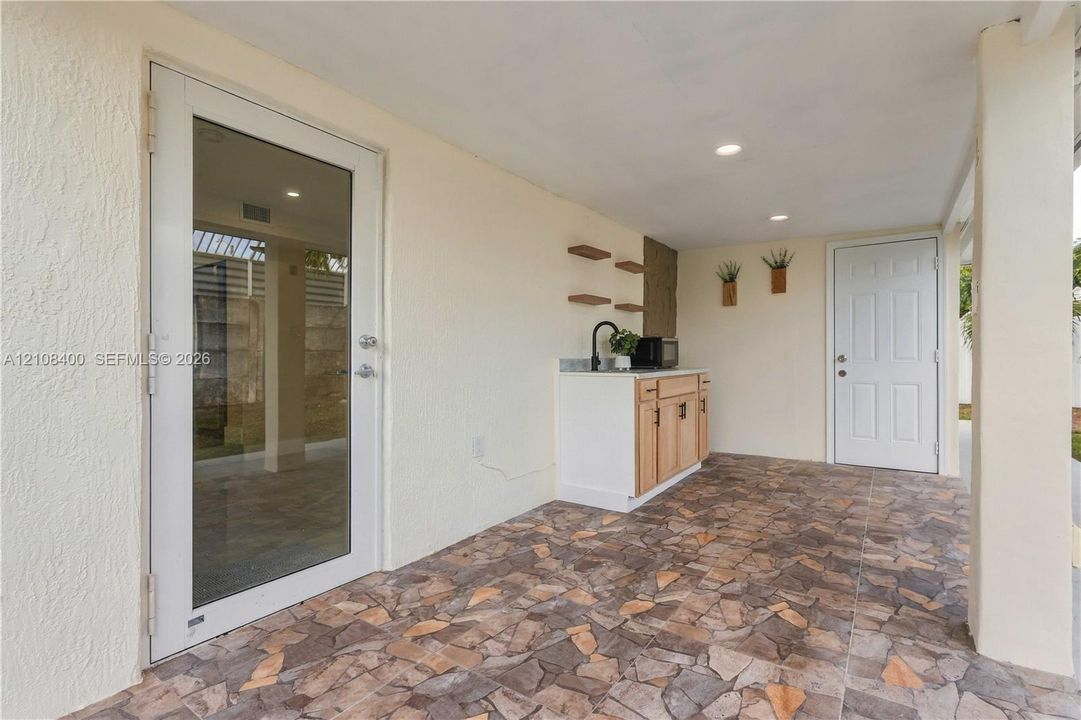 Covered patio featuring stone-tiled flooring, built-in cabinetry with a sink, recessed lighting, and a glass-panel door
